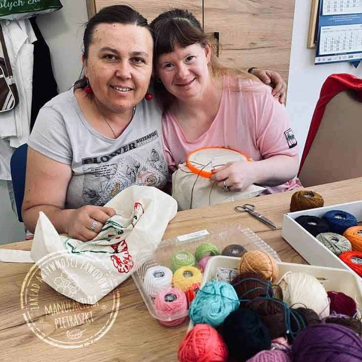 Dwie kobiety haftują przy stole z kolorowymi włóczkami