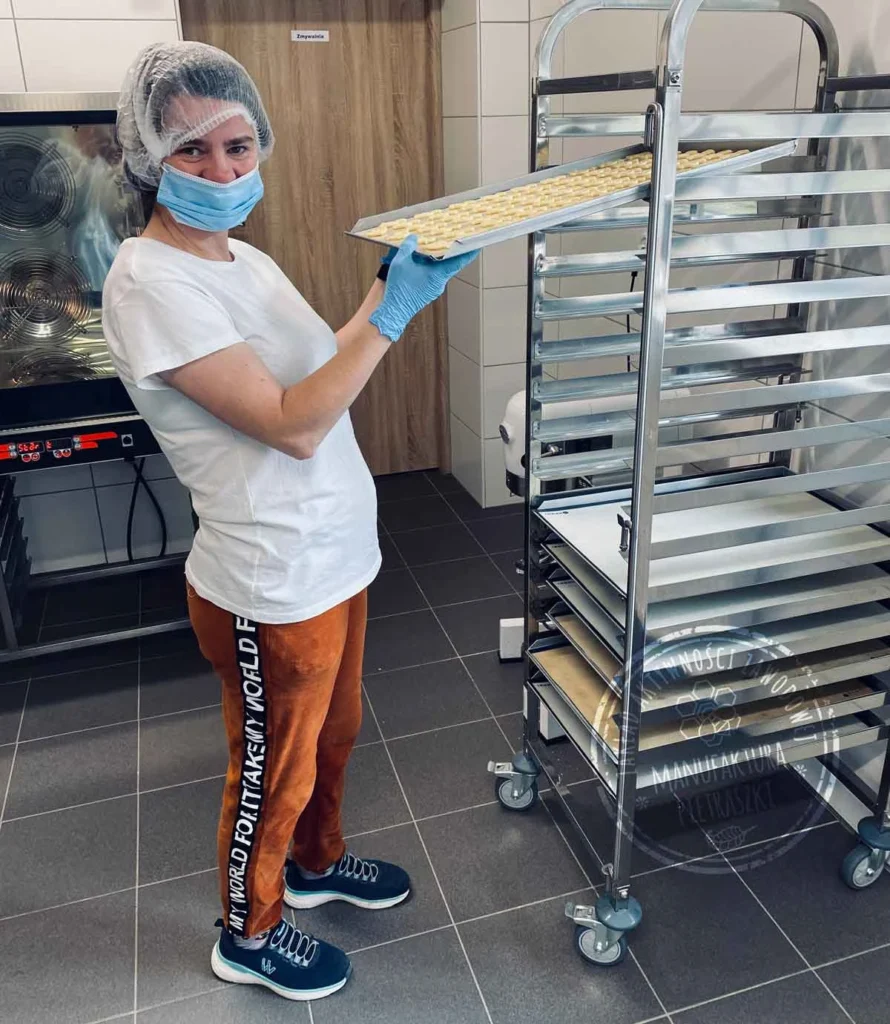 Kobieta trzyma blachę z ciastkami w pracowni cukierniczej